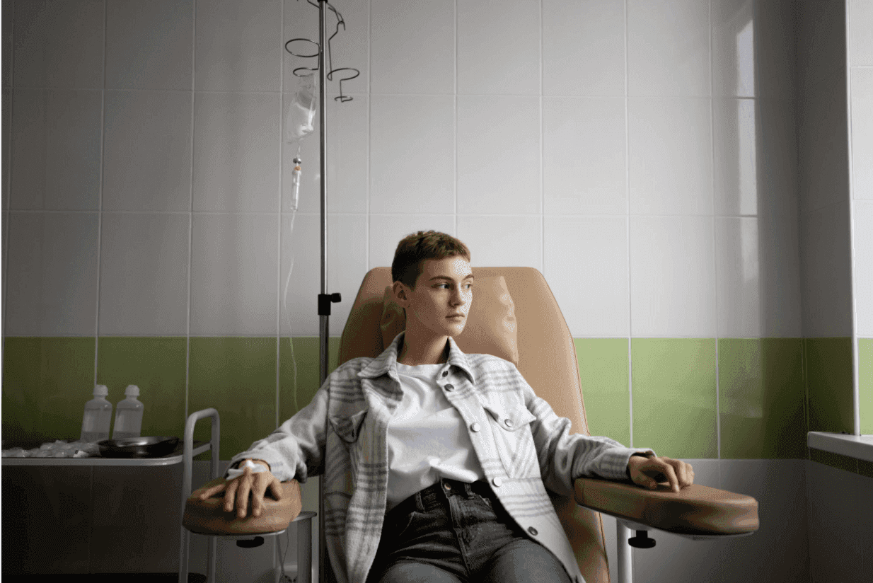 A patient in a plaid shirt sits in a medical chair receiving IV therapy.