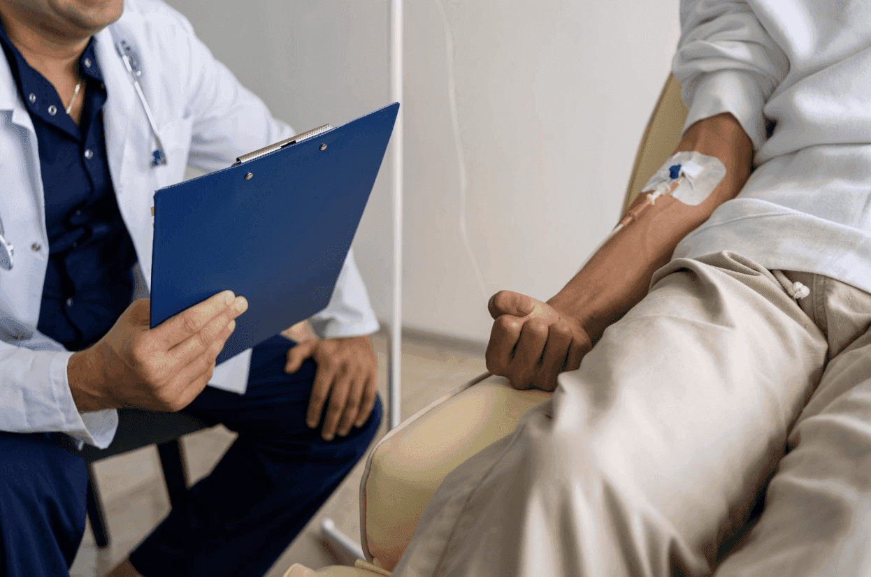 A doctor holds a clipboard while a patient has an IV