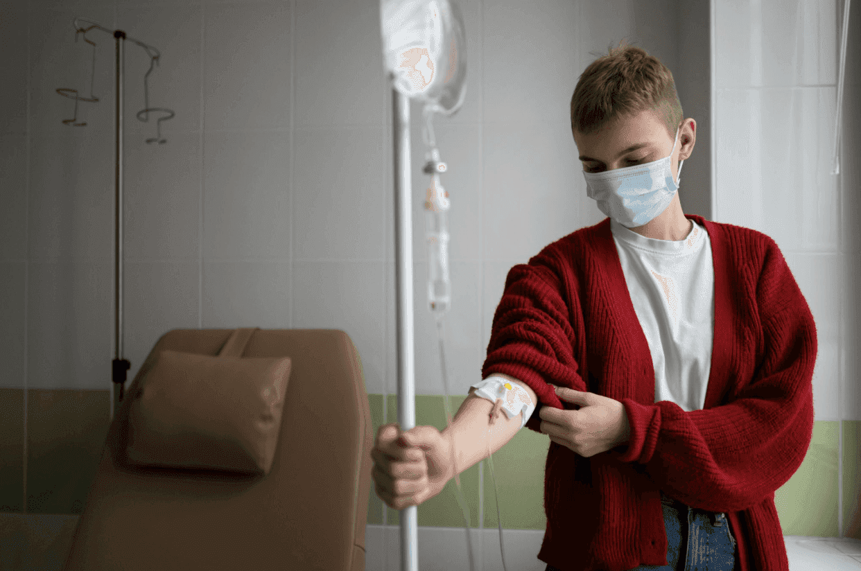 A patient wearing a face mask and a red sweater receiving IV treatment.