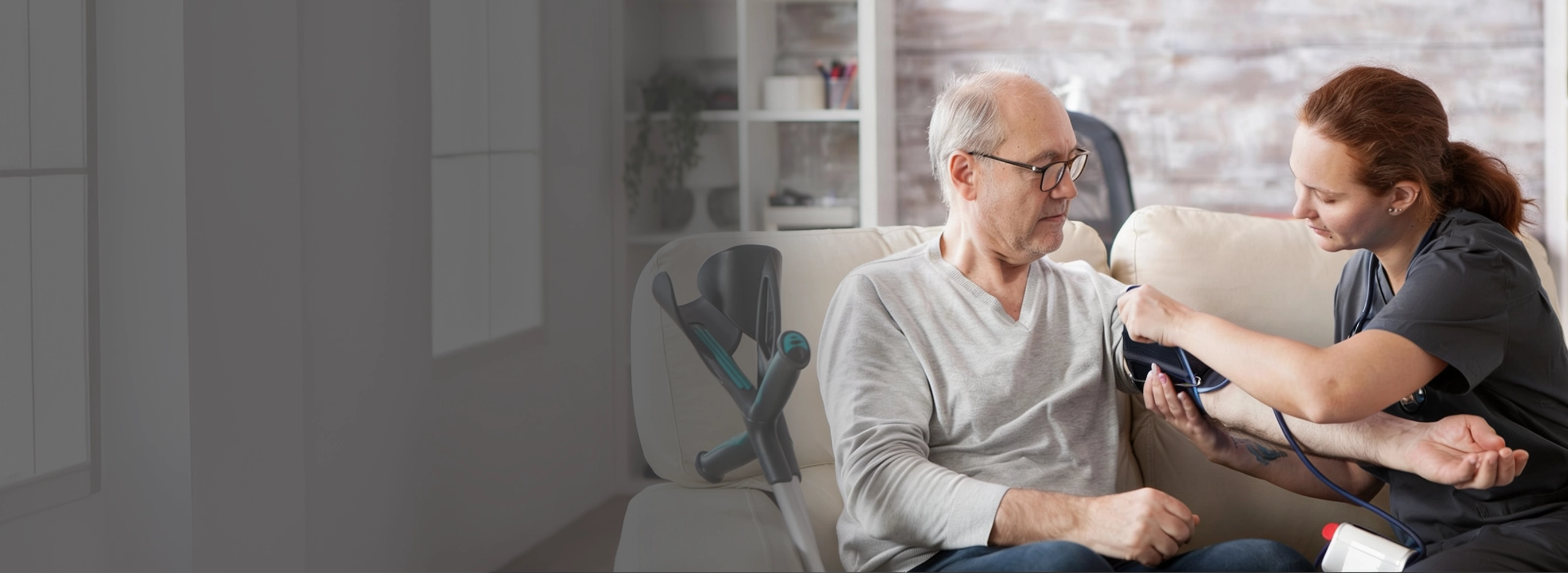 A female healthcare provider in scrubs checking an elderly male resident's blood pressure in an assisted living setting.