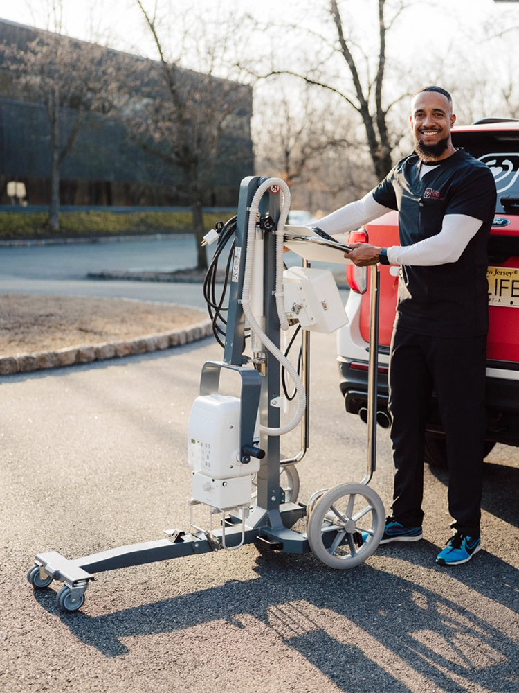 MobileCare technician with portable X-ray machine standing next to branded vehicle, providing in-home imaging services.